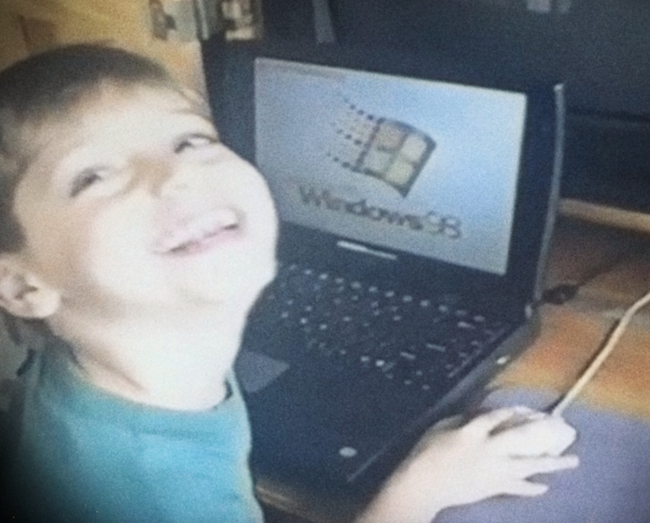 Bryan Bonilla Diaz as a child smiling at the camera while using a laptop with Windows 98.